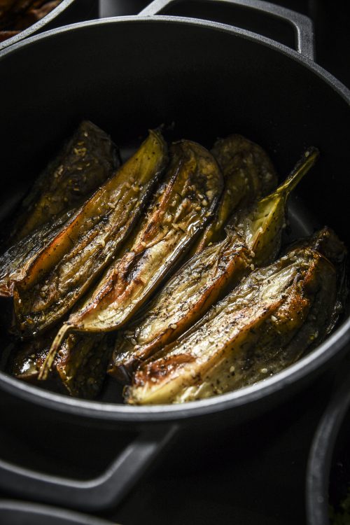 Aubergines coupées en deux et rôties dans une casserole noire, dorées et assaisonnées aux herbes.