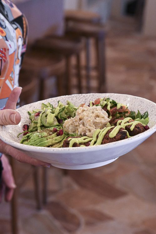 Personne tenant une assiette creuse garnie d’un bowl coloré avec crudités, falafels et sauce.