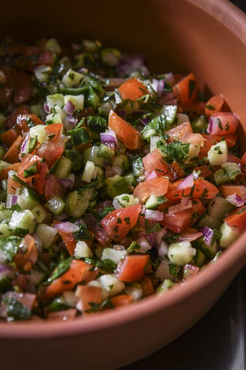 Mélange de concombre, tomate, oignon rouge et herbes fraîches dans un plat en terre cuite.