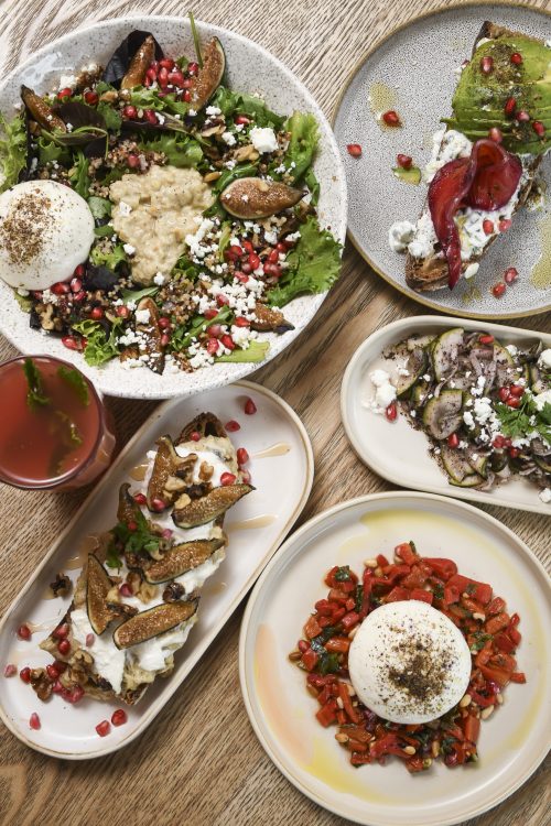 Vue du dessus de plusieurs assiettes colorées avec burrata, avocado toast, légumes, grenades et boissons.