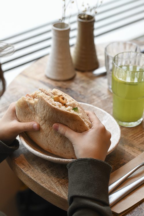 Pita Dip Honest Food tenue en main, garnie et généreuse, servie avec une boisson fraîche sur table en bois.